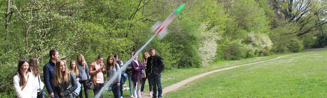 Eine Gruppe von Mädchen beim Testversuch mit einer kleinen Rakete in einem Park