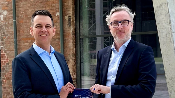 Two men in suits holding up a book together.