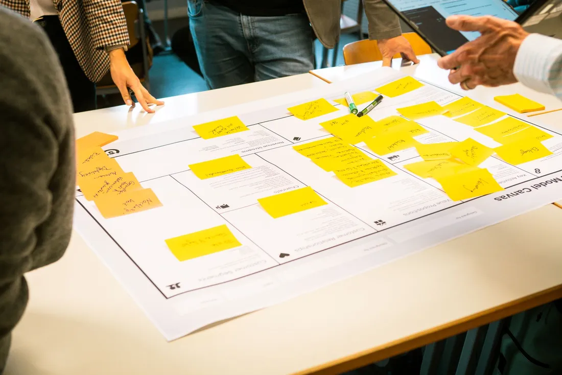 Hände mehrerer Personen an einem Tisch, einer zeigt auf ein Datenblatt in der Mitte