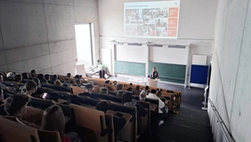 Zwei Herren vor einem vollen Hörsaal. 