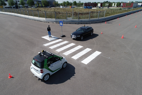 Abbildung von zwei autonom fahrender Fahrzeugen, die jeweils auf einer Seite eines Zebrastreifens stehen, den ein Dummy-Fußgänger überqueren möchte.