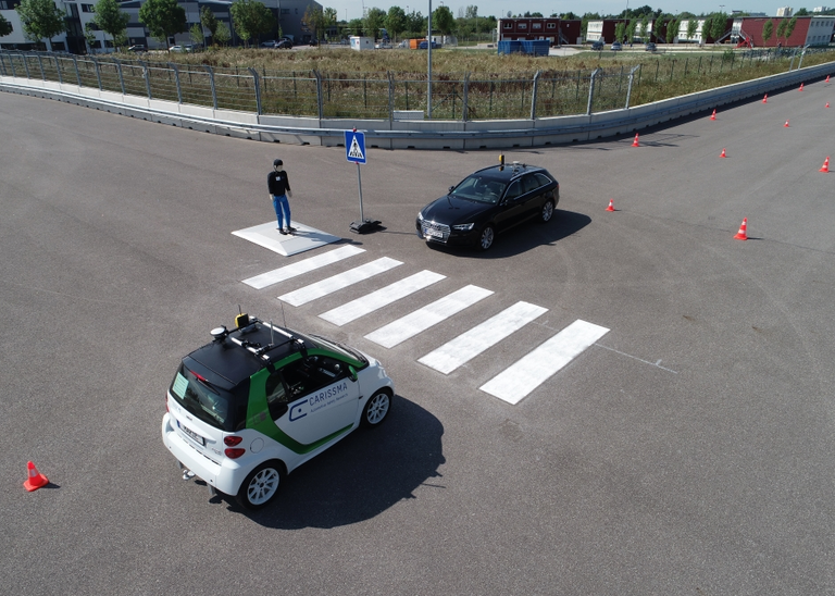 Abbildung von zwei autonom fahrender Fahrzeugen, die jeweils auf einer Seite eines Zebrastreifens stehen, den ein Dummy-Fußgänger überqueren möchte.