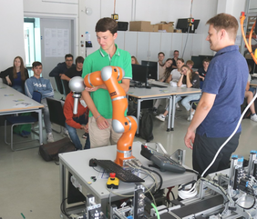 Student touches robot arm, together with professor and students in robotics lab