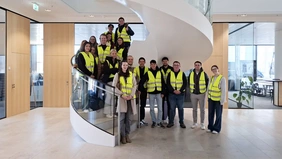 Group photo on a spiral staircase, all wearing yellow safety vests.
