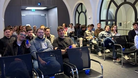 Eine Gruppe Menschen sitzt in einem bestuhlten Raum.