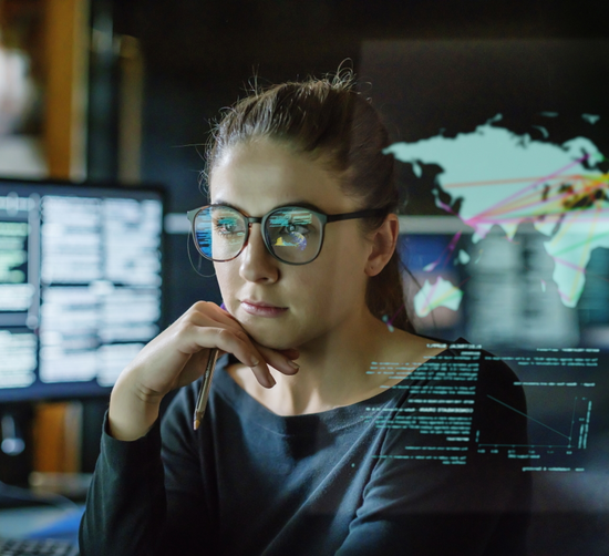 Junge Frau sitzt umgeben von Computerbildschirmen inmitten von Datenströmen/Zahlen/Grafiken 