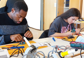 Students solder a robot together in the lecture hall