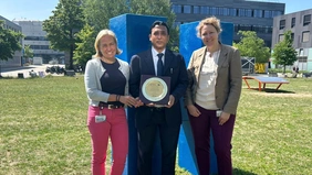 Three people are standing in a meadow and holding up a sign.  halten eine Plakette ins Bild 