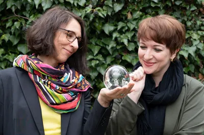 Zwei Frauen Blicken auf eine Glaskugel, die eine von beiden in der Hand hält