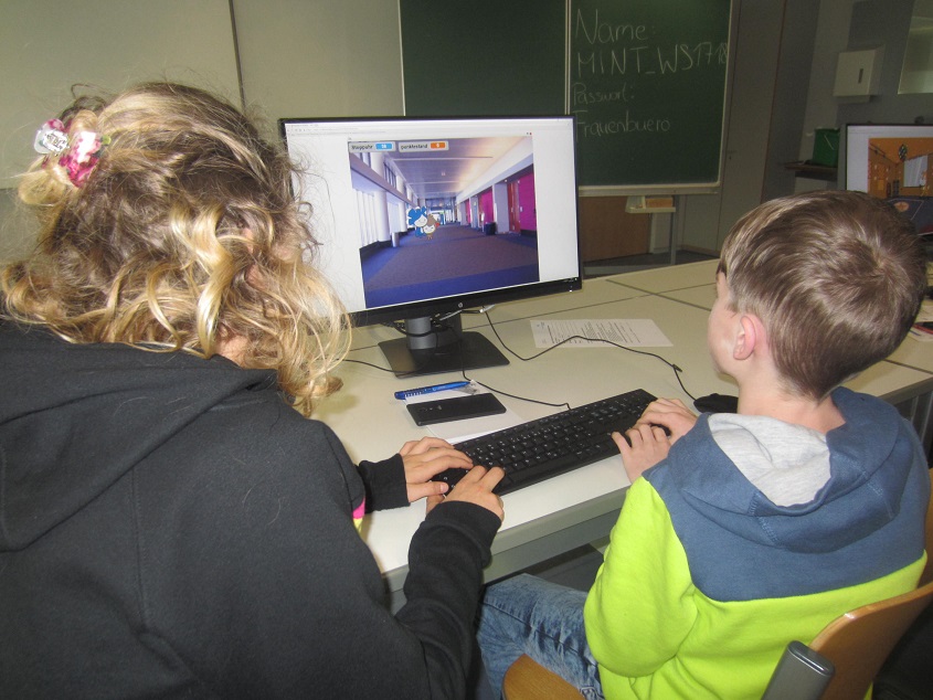 Zwei Kinder sitzen an einem Bildschirm und programmieren ein einfaches Computerspiel