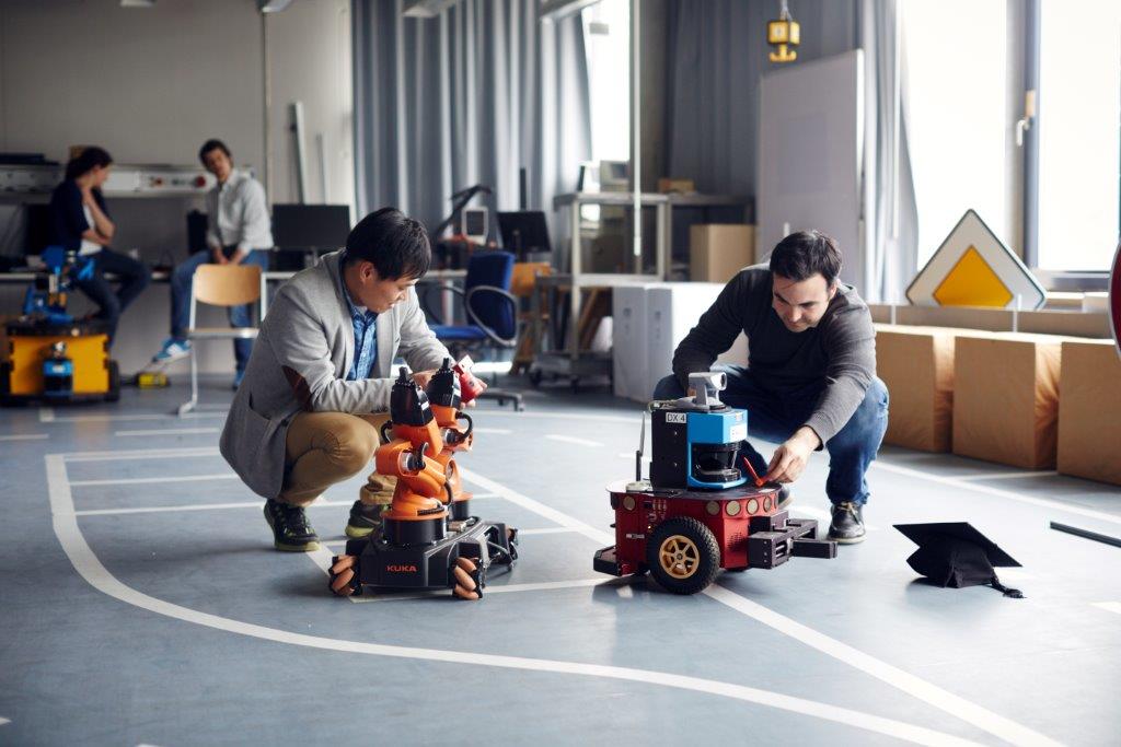 Quelle: THI Zwei Promovierende testen im Labor für Robotik zwei Roboter.