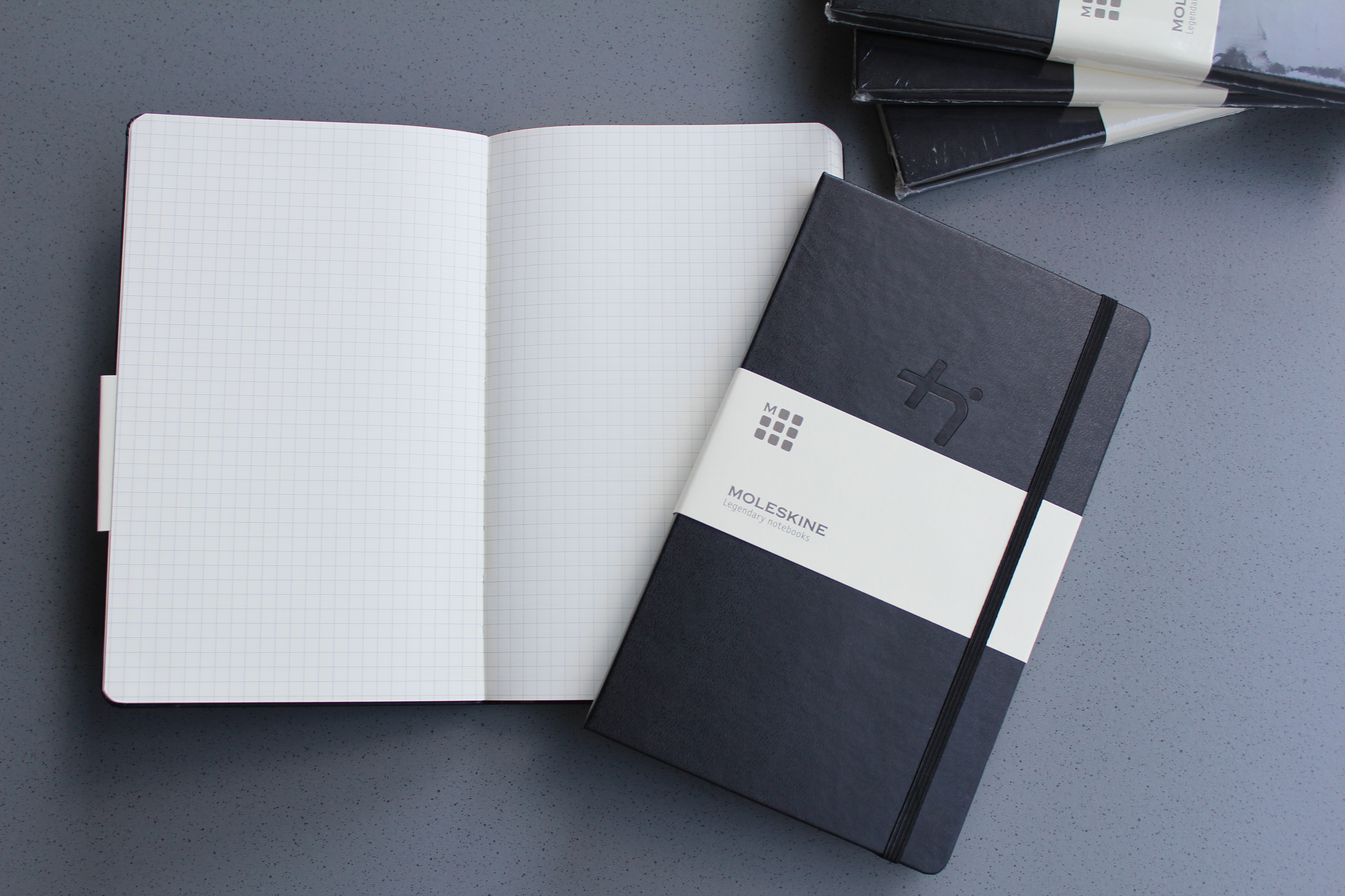 Ein geschlossenes Notizbuch mit schwarzem Einband liegt auf einem aufgeschlagenen Notizbuch