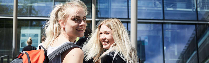 2 blonde Studentinnen blicken auf dem Weg ins THI-Gebäude zurück und lächeln