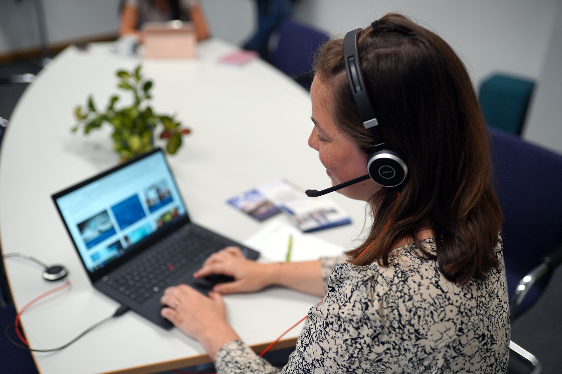 SChulterblick auf Frau mit Headset vor Laptop, Beratungssituation